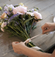Händer knyter ett band runt en bukett med färgglada blommor på ett bord.